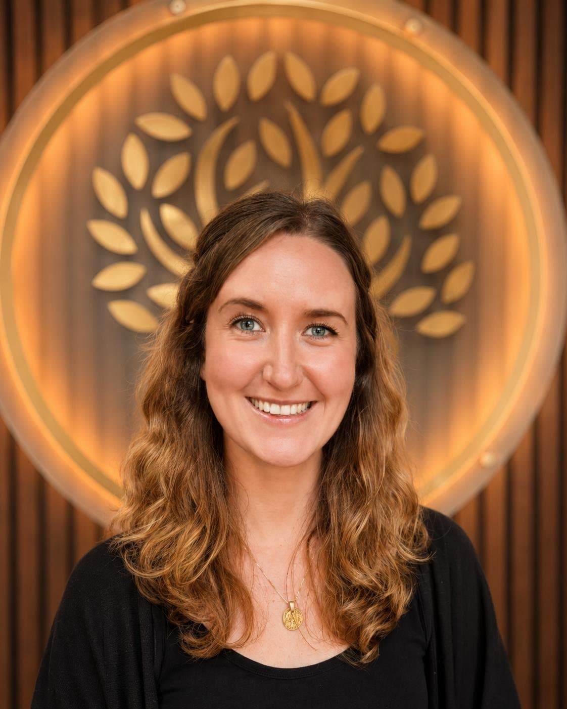 Tess Ellerbeck smiling in front of a golden tree-of-life wall light